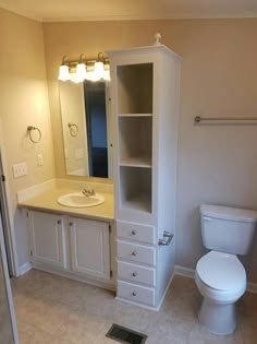 a white toilet sitting next to a bathroom sink under a mirror and a shelf above it