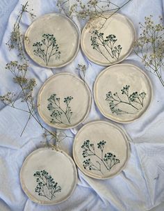 four plates with flowers on them sitting on a white cloth covered tablecloth, one is empty and the other has no leaves