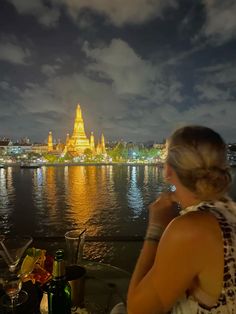 a woman sitting at a table looking out over the water with a city in the background