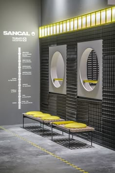 three benches are in front of two circular mirrors on the wall and below them is a sign that says sancali