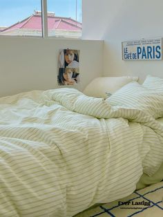 an unmade bed with white sheets and pillows in front of a window overlooking the city