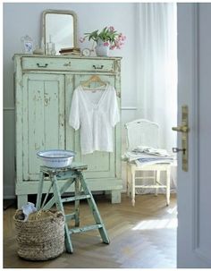 a room with an old dresser, chair and table in the corner that has a mirror on it