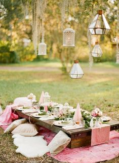 a picnic table with pink and white decor in the middle of a grassy area surrounded by trees