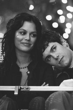 black and white photograph of two people sitting next to each other in front of christmas lights