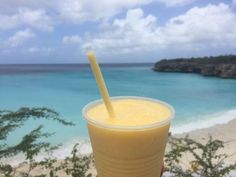 a person holding up a drink with a straw in front of the ocean and blue sky