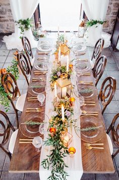 the table is set with candles, plates and greenery for an elegant dinner party