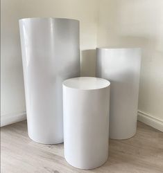 three white vases sitting next to each other on a wooden floor in front of a wall