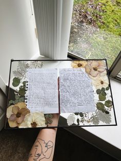 a person holding up a book with writing on it and flowers in front of them