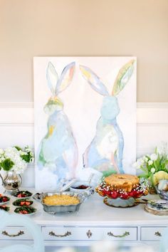 a table topped with cakes and desserts covered in frosting next to a painting