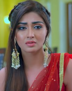 a woman with long hair wearing earrings and a red sari is looking at the camera