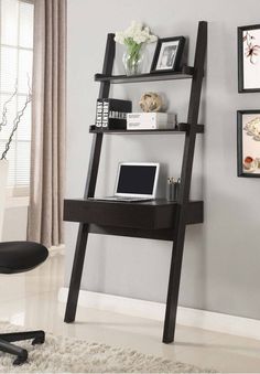 a desk with a laptop on top of it next to a chair and wall hangings