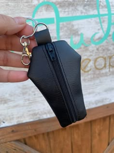 a hand holding a black purse keychain in front of a sign