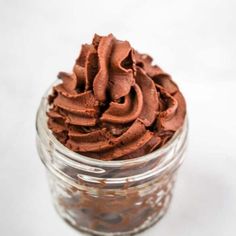 a glass jar filled with chocolate frosting on top of a white countertop next to a spoon