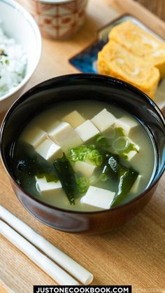 a bowl of soup with tofu, broccoli and rice on a wooden table