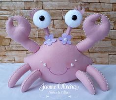 a pink stuffed crab with two eyes and flowers on it's head, sitting in front of a brick wall