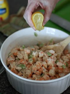 a person holding a lemon over a bowl filled with food