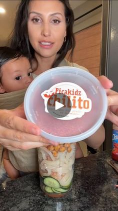 a woman holding up a plastic container with food in it next to a small child