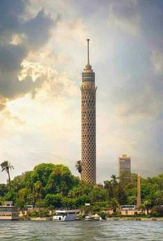 a tall tower sitting on top of a river next to a lush green forest covered hillside