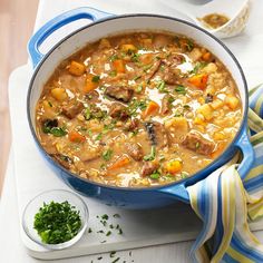 a blue pot filled with meat and vegetables on top of a white table next to a spoon