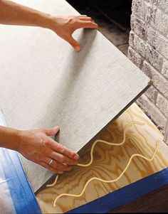 a person that is laying down some kind of flooring material on the ground in front of a brick wall