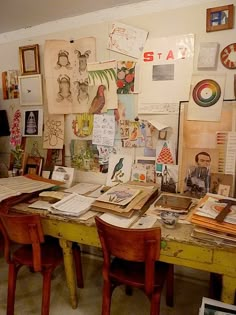 a desk with many papers and pictures on the wall next to some chairs in front of it