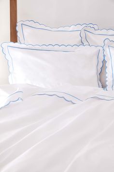 a bed with white sheets and blue scalloped trim on the pillowcases