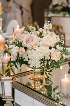 a vase filled with white and pink flowers sitting on top of a table next to candles