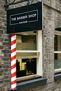 a barber shop sign hanging from the side of a brick building next to a window