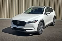 a white mazda cx - 5 is parked in front of a building with corrugated walls