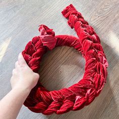 someone is making a wreath out of red fabric on the floor with their hands and fingers