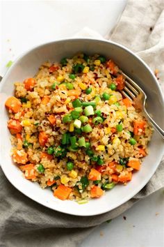 a white bowl filled with rice and vegetables on top of a cloth next to a fork