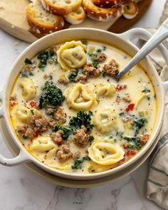 a bowl of pasta with meat and spinach in it next to bread on a cutting board