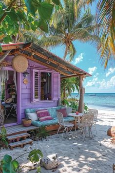 a small purple hut on the beach with chairs and tables in front of it, surrounded by palm trees