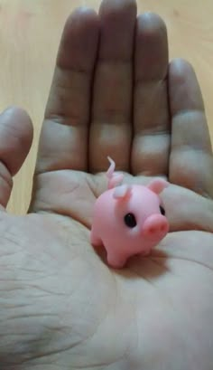 a small pink pig toy sitting in the palm of someone's hand