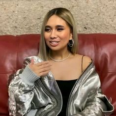 a woman sitting on top of a red couch wearing a silver jacket and black dress