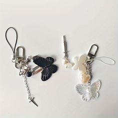 two key chains with charms attached to them on a white surface, one is shaped like a butterfly and the other has a cross