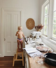 a toddler standing on a stool in front of a kitchen counter with pots and pans