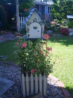 a bird house with flowers growing in it's planter next to a fence