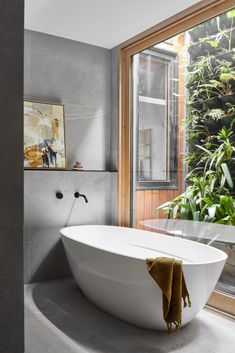 a bath tub sitting next to a window in a room with plants on the wall