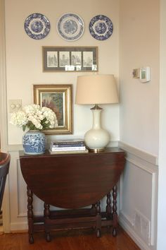 a table with a lamp, vase and pictures on the wall above it in a living room