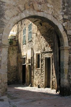 an old stone building with green shutters on the door and windows in between two archways