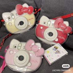 two hello kitty cameras sitting next to each other on top of a bed with pink bows