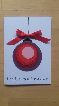 a christmas ornament hanging from a red ribbon on a white card with the words, frohe weinhacht