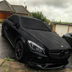 a black mercedes cla parked in front of a house on a rainy day with no one around