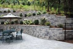 an outdoor patio with tables and umbrellas in the middle of it, surrounded by stone walls