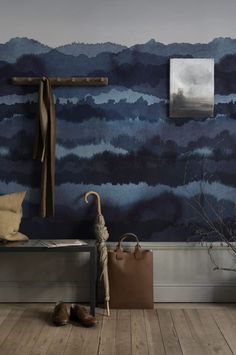 a wooden bench sitting in front of a wall covered in blue watercolors with a cross hanging on it