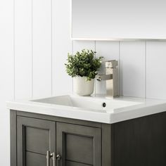 a white sink sitting under a mirror next to a wooden cabinet with a plant in it