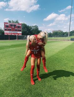 two girls in red soccer uniforms are hugging each other on the field at a baseball game