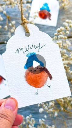 someone holding up a card with a bird on it and the words merry written in blue