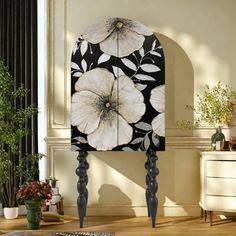 a black and white clock with flowers painted on it's face in the middle of a room